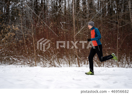 Photo of running athlete among trees in winter forest 46956682