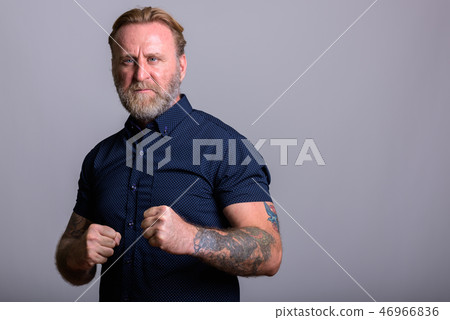 Studio shot of mature bearded man with hand tattoos getting read Studio shot of mature bearded man with hand tattoos getting read 46966836