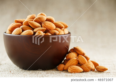 Almonds in a wooden cup on a burlap cloth . Almonds in a wooden cup on a burlap cloth . 46971007