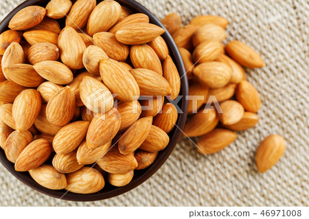Almonds in a wooden cup on a burlap cloth . 46971008