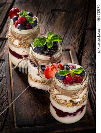 Tasty yoghurts with muesli, fresh berries and jam on wooden table. 46978976