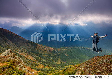 Young man jumping on top of a mountain against the sky 46981564