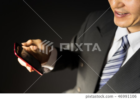 Incompetent businessman who smiles while looking at the smartphone 46991106