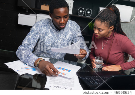 two young black people discuss their business using diagrams sitting at Desk in the office 46998634