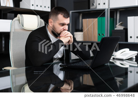 Portrait of young man sitting at table in office Portrait of young man sitting at table in office 46998648