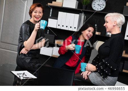 Three business women talking with coffee in hand in stylish office 46998655