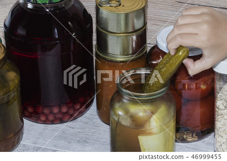 hand reaching for pickled cucumber. Storage shelves in pantry with homemade canned preserved fruits hand reaching for pickled cucumber. Storage shelves in pantry with homemade canned preserved fruits 46999455