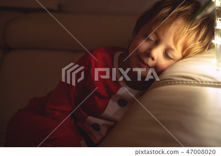 Beautiful boy sleeps on the sofa in Christmas night. Child sleeping under a Christmas tree Beautiful boy sleeps on the sofa in Christmas night. Child sleeping under a Christmas tree 47008020