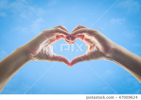 Heart shape woman hands against blue sky backgroun 47009624