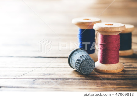 Wooden reel with thread and fingertip close-up. Wooden reel with thread and fingertip close-up. 47009818