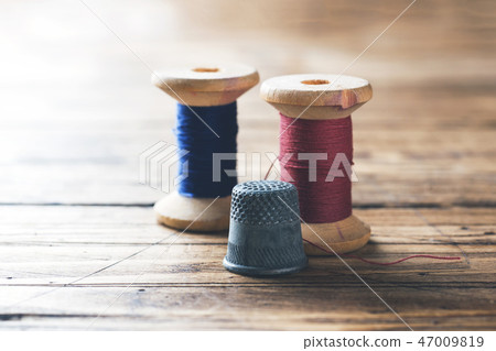 Wooden reel with thread and fingertip close-up. Wooden reel with thread and fingertip close-up. 47009819