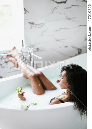 Young black girl lying in bathroom with marble tile and relaxing. 47010896