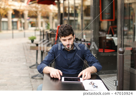 Disgruntled man playing online game by tablet at street cafe. Disgruntled man playing online game by tablet at street cafe. 47010924