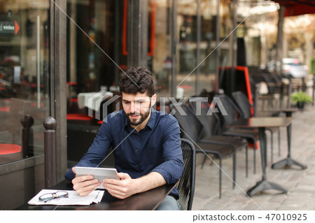 Disgruntled man playing online game by tablet at street cafe. Disgruntled man playing online game by tablet at street cafe. 47010925