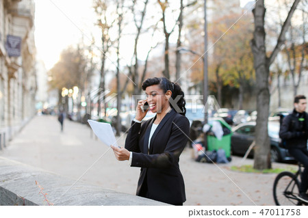 Marketer got raise, pretty lady standing on street with papers i 47011758