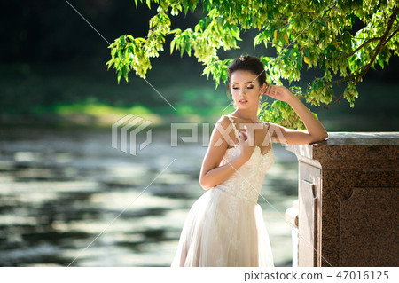 fashion photo of beautiful woman with dark hair in luxurious wedding dress posing outdoor. fashion photo of beautiful woman with dark hair in luxurious wedding dress posing outdoor. 47016125