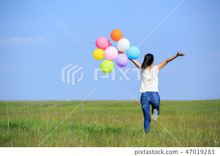 running and jumping with colored balloons outdoors 47019283