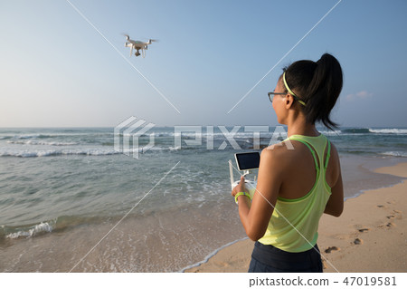 Woman  remote control a drone on seaside 47019581