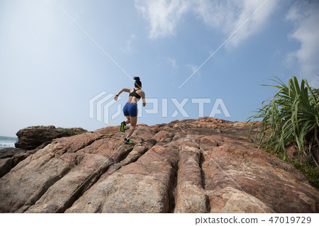 Woman trail runner running to rocky mountain top  47019729