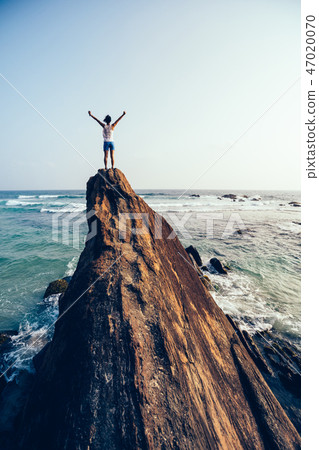young woman open arms on seaside rock cliff edge 47020070