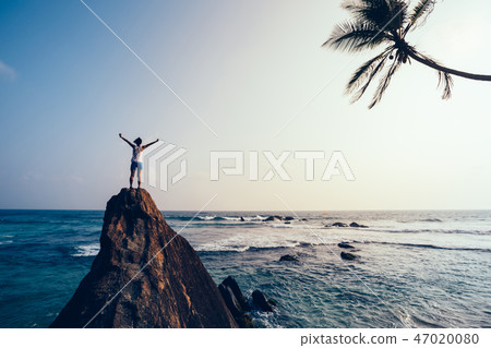 young woman  open arms on seaside rock cliff edge 47020080