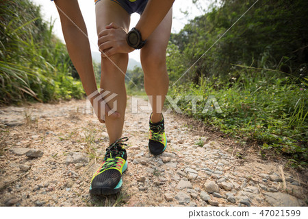 runner hold her sports injured leg on rocky trail 47021599