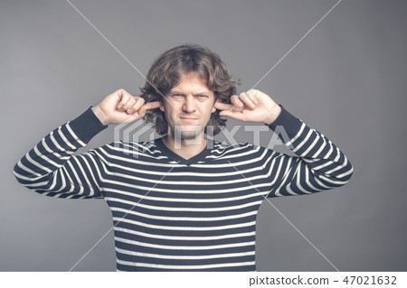 Displeased man plugging ears with fingers doesn't want to listen anything isolated on gray wall 47021632