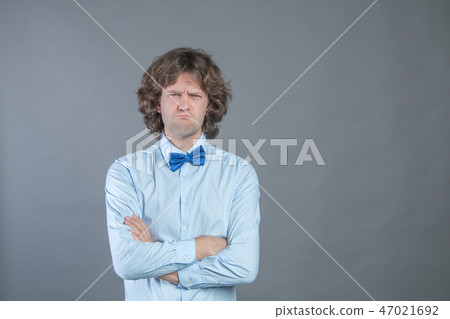 Resentful man with arms folded over gray background in studio shot and offended looked at camera Resentful man with arms folded over gray background in studio shot and offended looked at camera 47021692