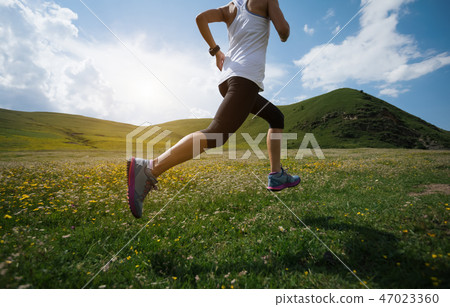 Young fitness woman trail runner running grassland 47023360