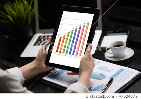 Close-up hands holding tablet on background of financial documents 47024372
