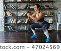 Woman doing squat workout and smiling during fitness training at home 47024569
