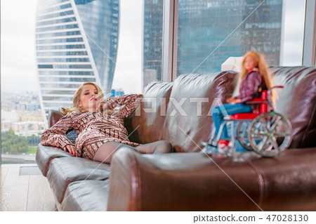 A beautiful young blonde girl in a fashionable dress with a disability, posing on a leather sofa A beautiful young blonde girl in a fashionable dress with a disability, posing on a leather sofa 47028130