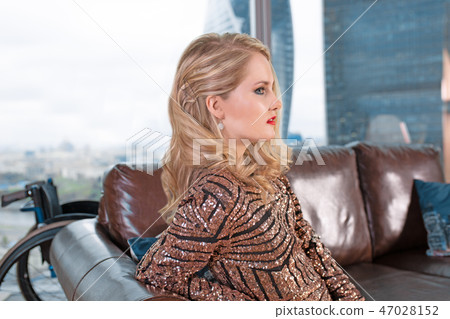 A beautiful young blonde girl in a fashionable dress with a disability, posing on a leather sofa A beautiful young blonde girl in a fashionable dress with a disability, posing on a leather sofa 47028152