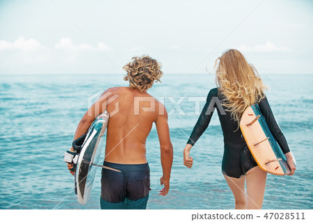 Surfers at the beach- Smiling couple of surfers walking on the beach and having fun in summer Surfers at the beach- Smiling couple of surfers walking on the beach and having fun in summer 47028511