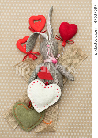 Rabbit handmade with red and white hearts lying on cardboard background in white peas Rabbit handmade with red and white hearts lying on cardboard background in white peas 47037097