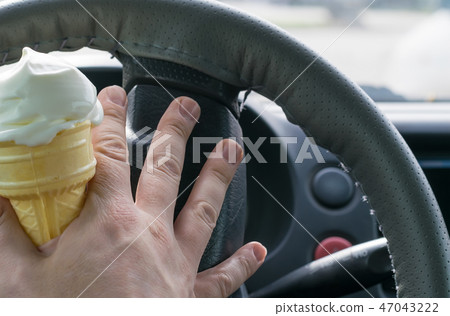 man holding ice cream behind the wheel of a car 47043222