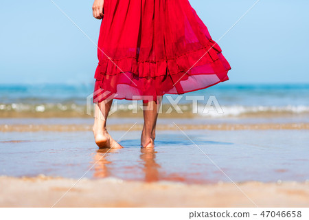 Woman walking by the seaside wearing red dress 47046658