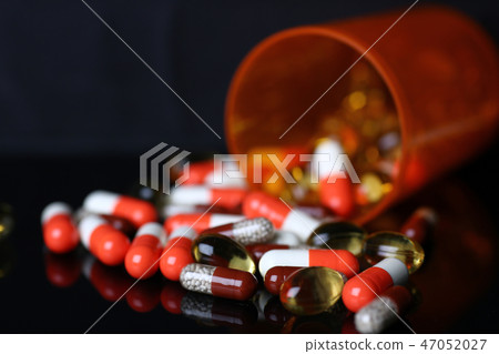 Pile of pills fall out from jar on black background Pile of pills fall out from jar on black background 47052027