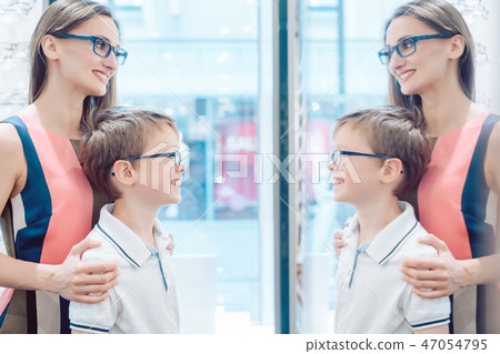 Mother and her son testing new glasses in the mirror Mother and her son testing new glasses in the mirror 47054795