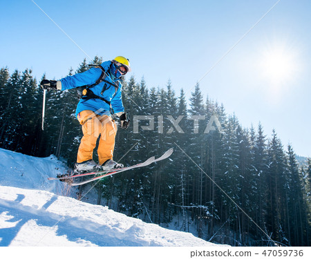 Professional skier jumping in the air while skiing in the mountains blue sky on the background 47059736