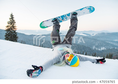 Excited young snowboarder woman having fun on the slope lying on the snow with her legs in the air 47059765