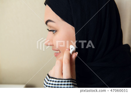 Portrait of a young and attractive muslim woman in a turban or hijab listening to streaming music on Portrait of a young and attractive muslim woman in a turban or hijab listening to streaming music on 47060031