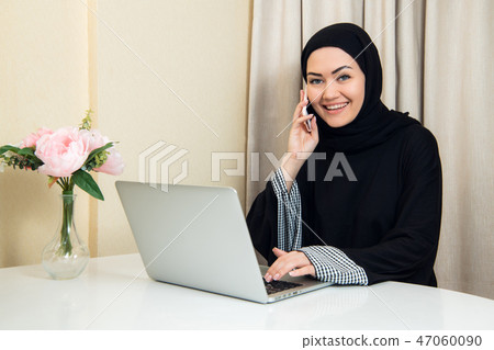 Muslim female talking on the phone while working with laptop computer. 47060090