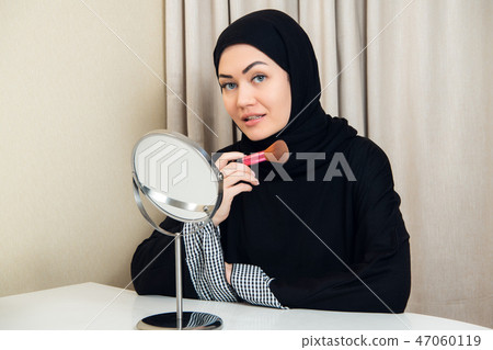 Arab woman applying makeup on her face, wearing traditional Arabian dress 47060119