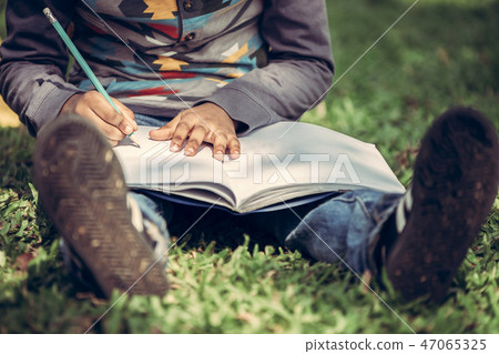 Little child writing on a notebook in the park. 47065325