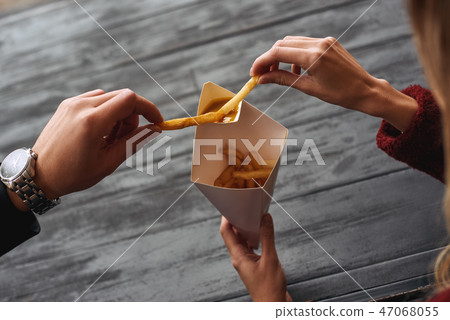 Close-up of young couple are eating french fries at the street food market. Close-up of young couple are eating french fries at the street food market. 47068055
