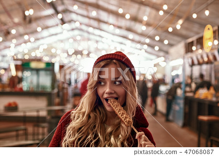 Close-up of young blonde woman eatting vegan sausage in dough Close-up of young blonde woman eatting vegan sausage in dough 47068087