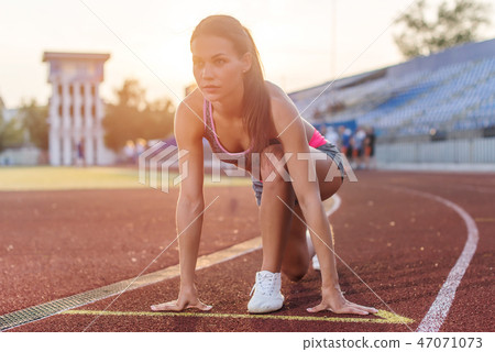 Women sprinters at starting position ready for race on racetrack. 47071073