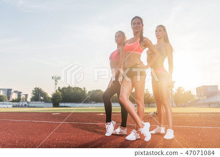 Group of fit young sportswomen standing in athletics stadium and posing. 47071084