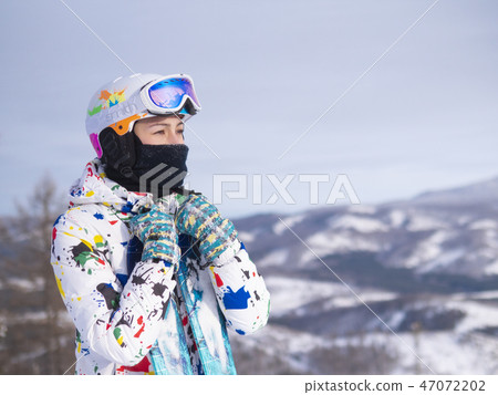 girl holding skis in her hands Happy girl holding skis and ski poles in hands, sitting in snow 47072202